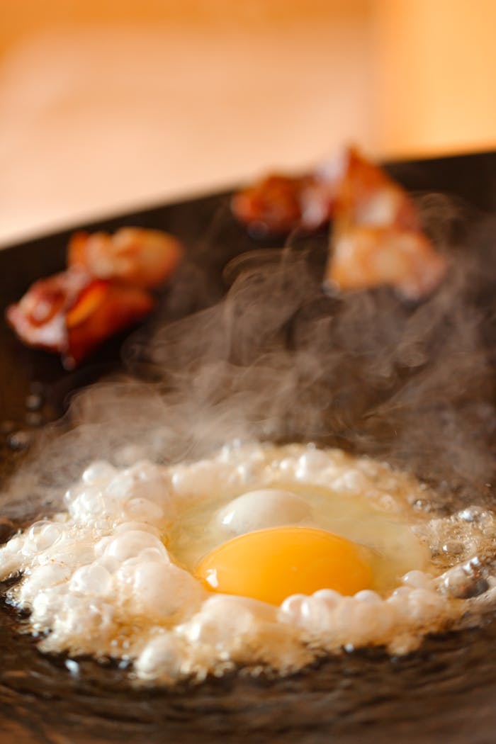 Steaming fried egg with crispy bacon in a hot skillet, perfect for breakfast.