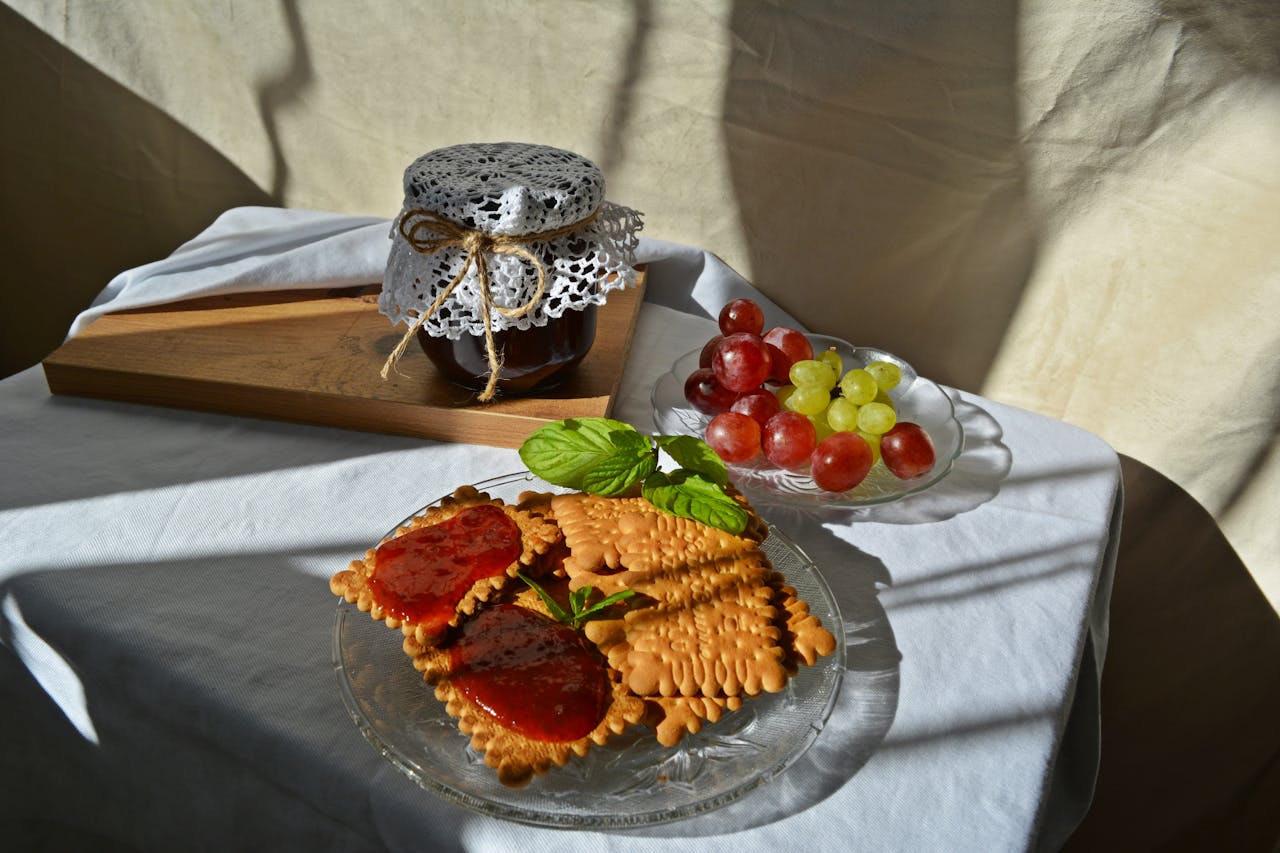 Plate of biscuits with fruit jam and grapes creates a perfect breakfast scene.