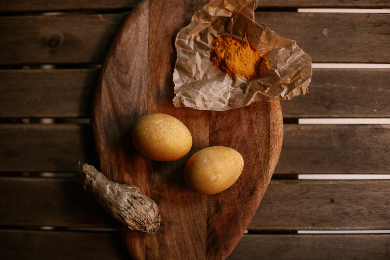 Top view of brown eggs, ginger, and spices on a wooden board.