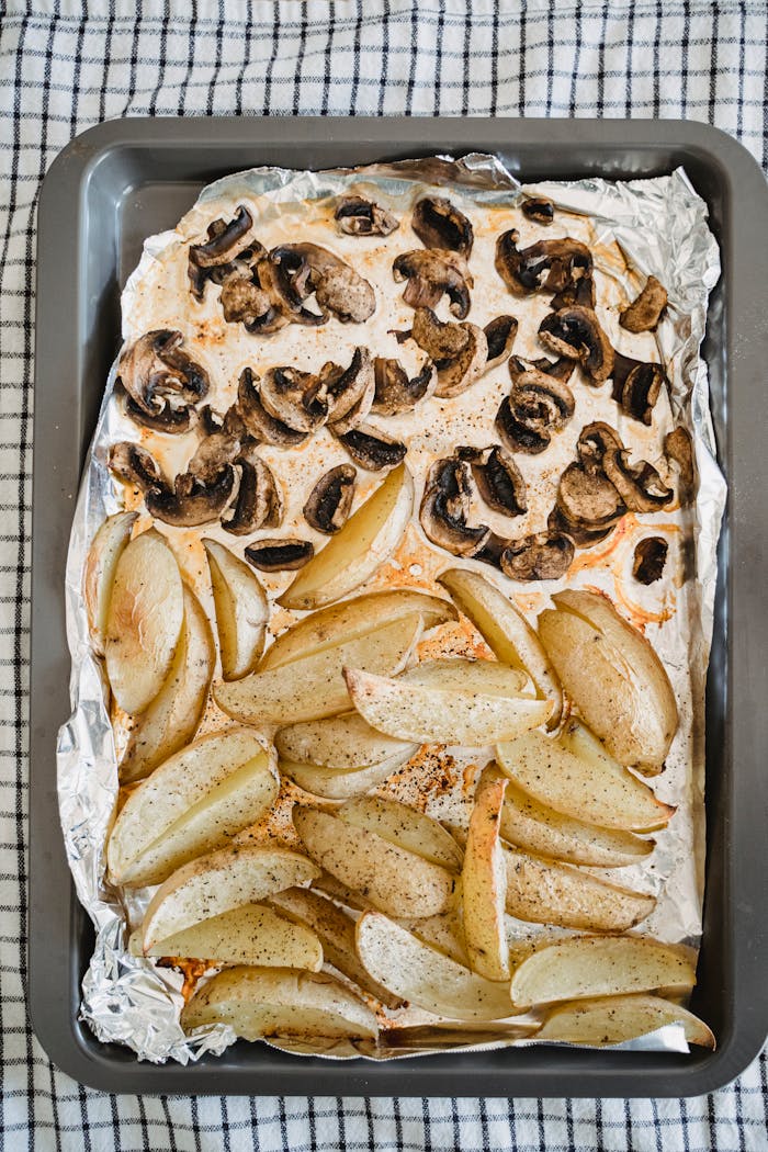 Top view of roasted potato wedges and mushrooms on a baking tray with foil.